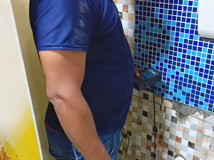 Técnico com geofone encostado na parede de pastilhas de um banheiro