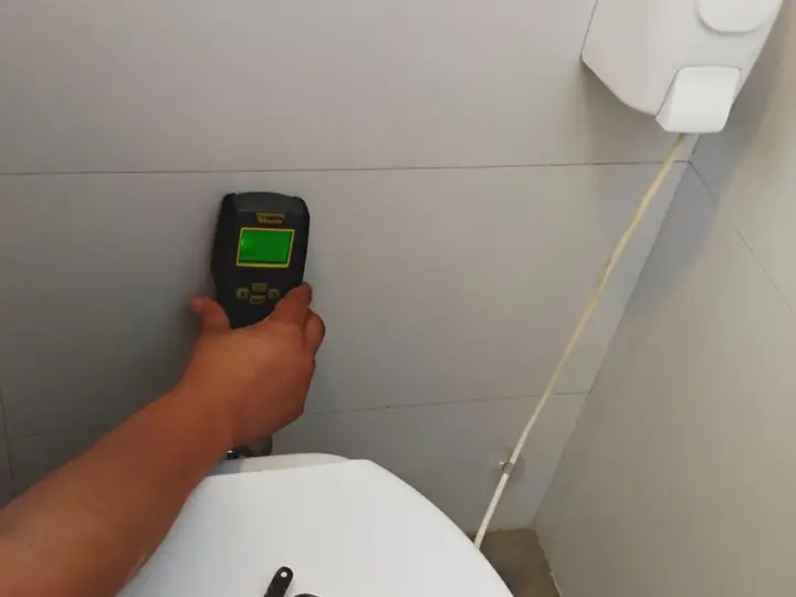 Medidor de umidade encostado na parede de azulejo atrás do vaso sanitário