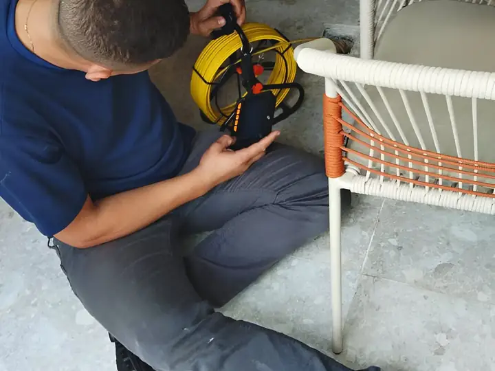 Técnico sentado no piso de um salão preparando a câmera de inspeção