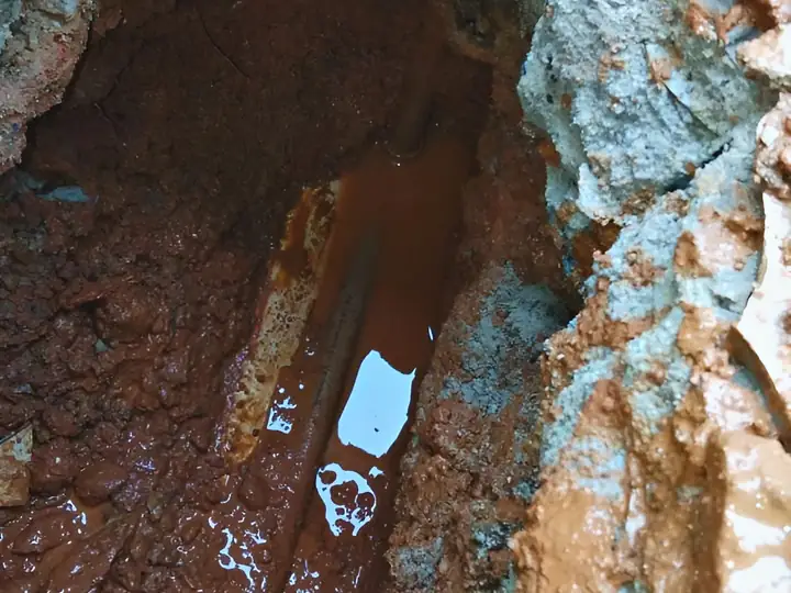 Abertura no piso com água acumulada e o cano danificado à mostra